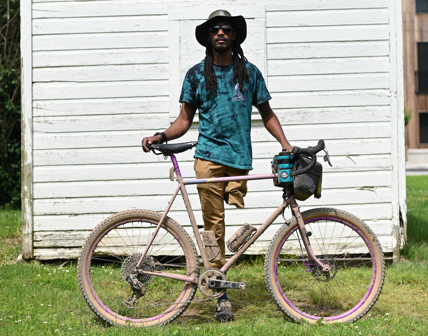 Leo Rogers, a black man with one leg, stands suavely with his bike against a white shed
