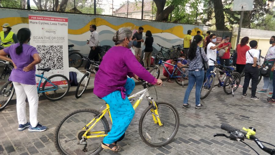 Woman cycling on a busy pedestrian street in Bengaluru, a mural is on a wall in the background